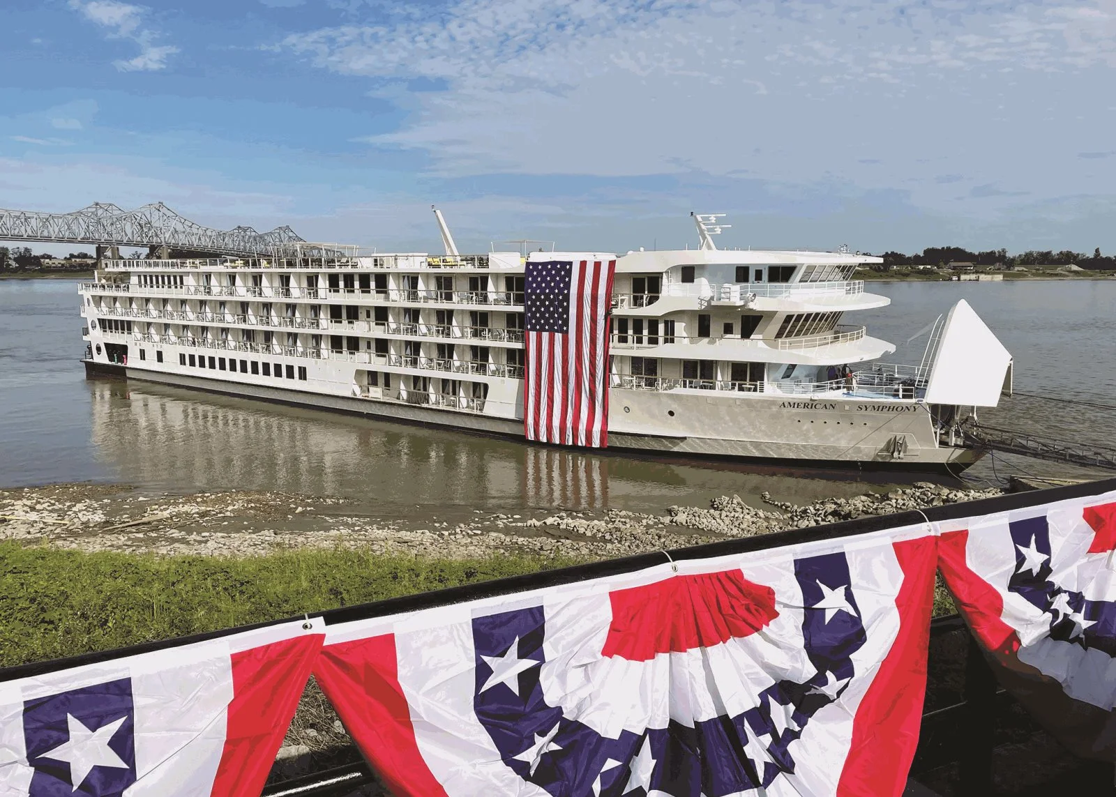 American Symphony riverboat docked with large American flag flying and patriotic bunting displayed